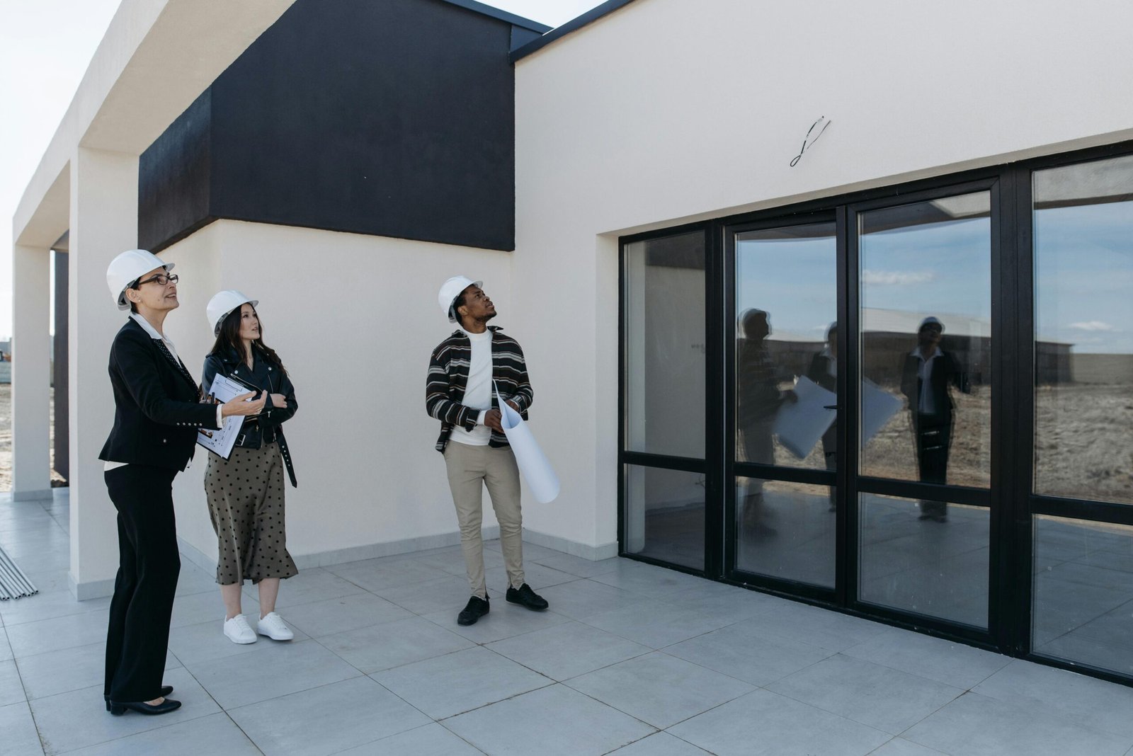 Architects in hard hats discuss the structure of a new building with large glass doors, suggesting a modern architectural design.